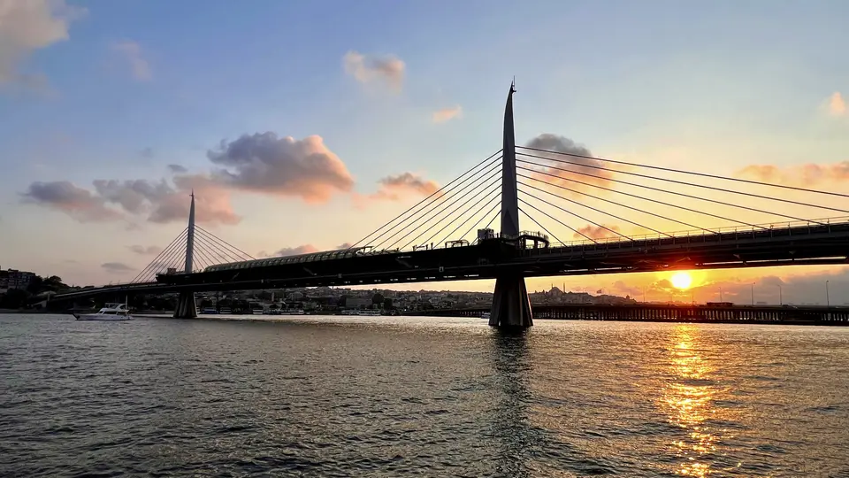 The Golden Horn Metro Bridge spans rippling water at sunset beneath a sky of pink clouds.