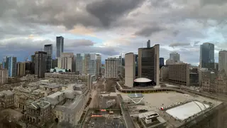 A cloudy aerial view of downtown high-rise buildings overlooks Toronto City Hall and an outdoor skating rink.