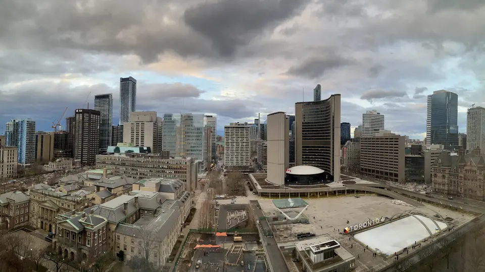 A cloudy aerial view of downtown high-rise buildings overlooks Toronto City Hall and an outdoor skating rink.