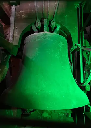 A large metal bell hangs within its mechanical frame under vivid green lighting.