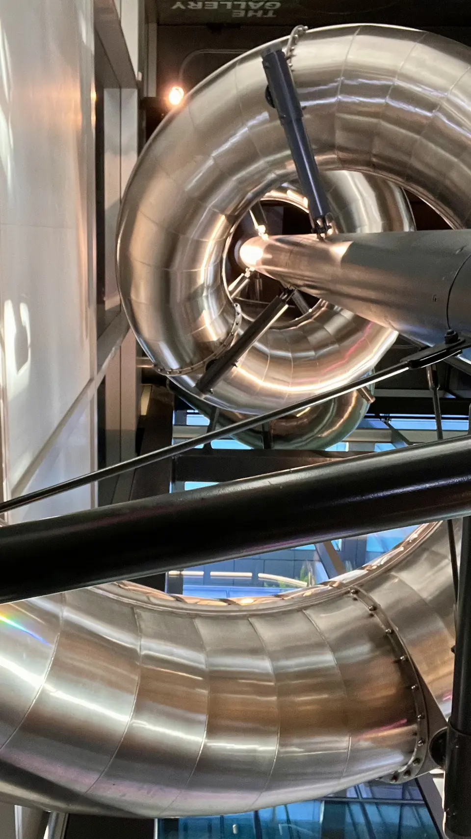A shiny metal tube slide curves through an indoor structure with black support rails.