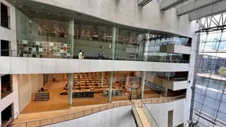 A multi-level modern library interior with glass walls, study tables, bookshelves, and a large windowed atrium overlooks the water.
