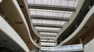 A modern multi-story interior atrium features curved balconies beneath a large gridded skylight.