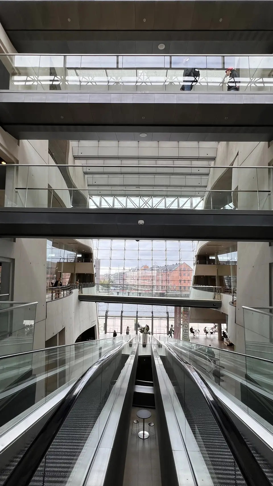 Escalators descend through a bright multilevel atrium with glass railings and large windows.