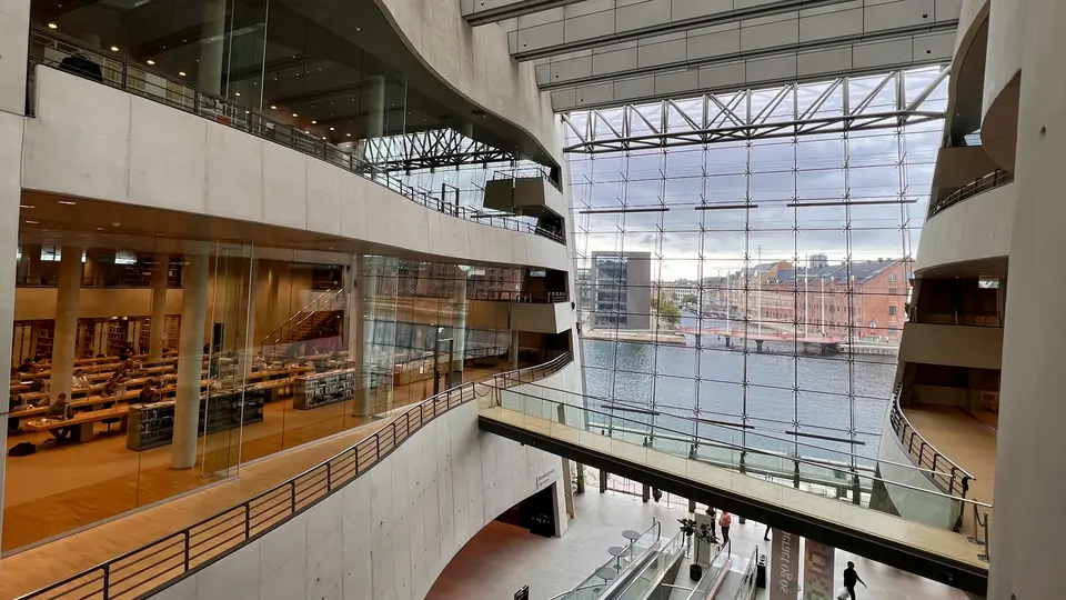 A spacious multi-level atrium with curved balconies, glass walls, and a large window overlooking a waterfront street.