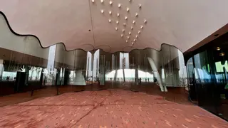 A curved glass entrance beneath a scalloped canopy opens onto a red brick plaza with small ceiling lights.