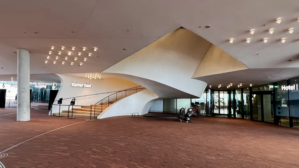 A sweeping white spiral staircase stands beneath a low ceiling with clustered lights in a modern building entrance.
