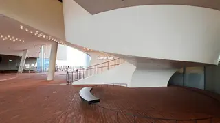 A sweeping white curved staircase and brick-floored ramp sit beneath a modern ceiling, with a sign reading "Kleiner Saal."
