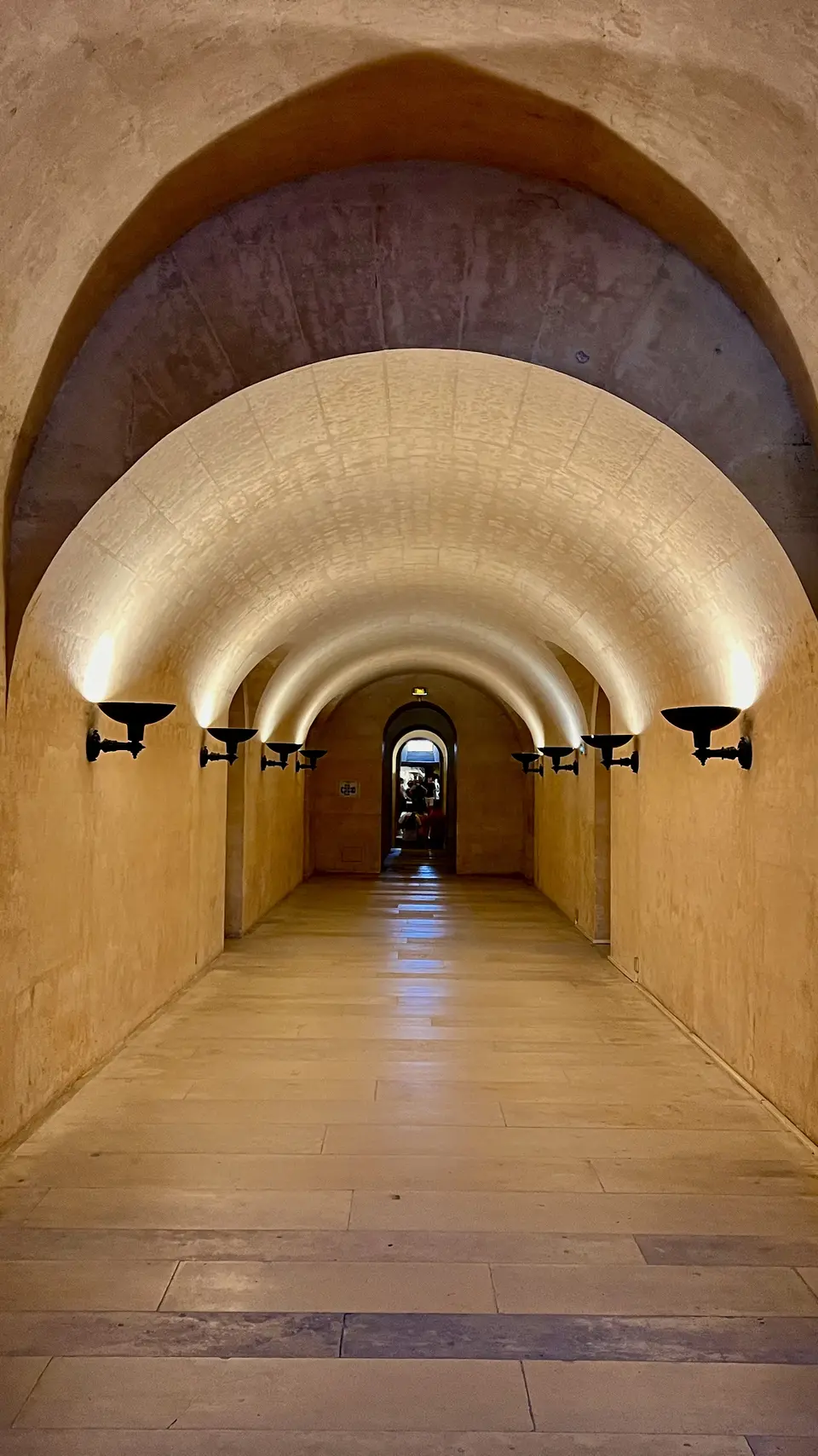 A warmly lit stone corridor with a series of rounded vaulted arches leads to a distant doorway.