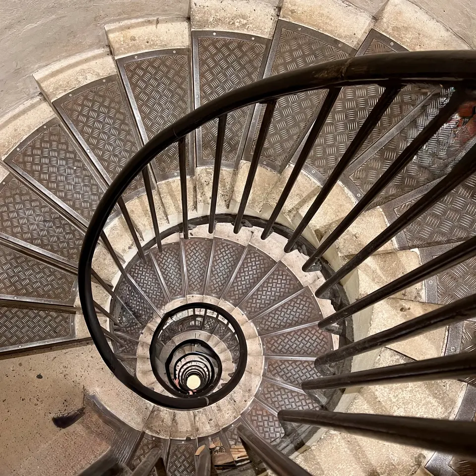 A black metal railing curves around a narrow spiral staircase with patterned metal treads.