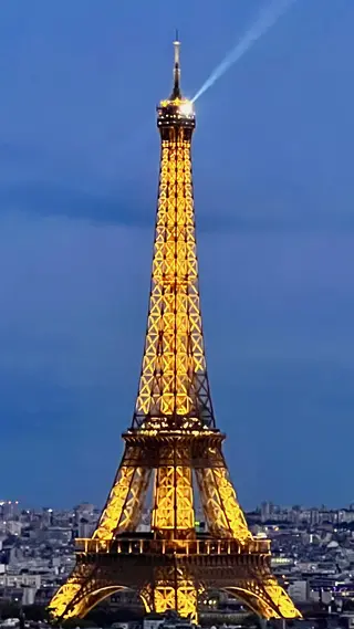 The Eiffel Tower glows with golden lights against a blue evening sky above the Paris skyline.