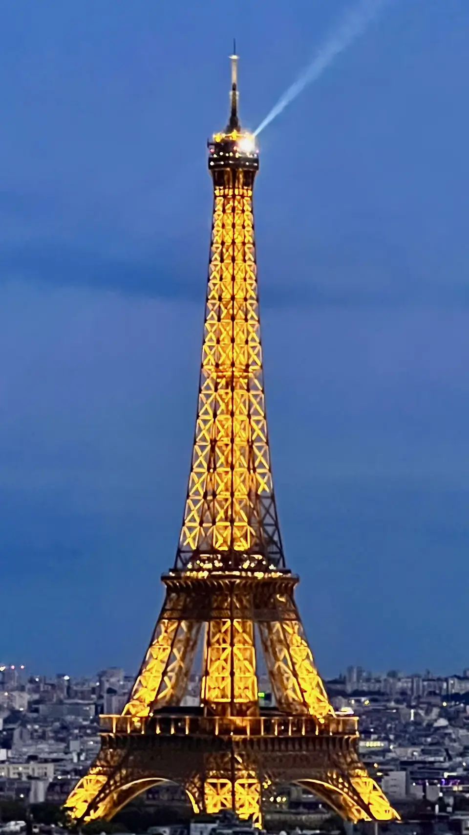 The Eiffel Tower glows with golden lights against a blue evening sky above the Paris skyline.