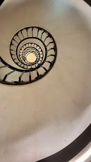 A black metal spiral staircase winds upward around a central opening against a pale wall.