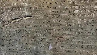 A weathered stone slab is covered with rows of carved cuneiform inscriptions.