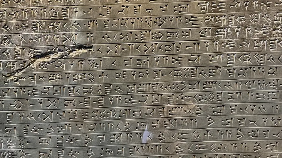 A weathered stone slab is covered with rows of carved cuneiform inscriptions.