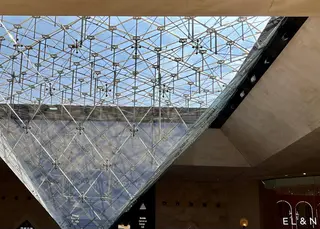 A sweeping glass-and-metal canopy with a geometric lattice rises above a warmly lit interior entrance.