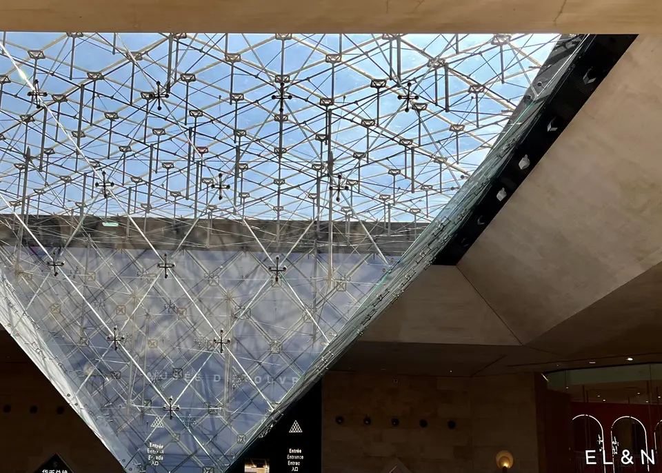 A sweeping glass-and-metal canopy with a geometric lattice rises above a warmly lit interior entrance.
