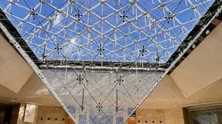A geometric glass skylight with a dense lattice of metal supports spans the ceiling above a modern interior.