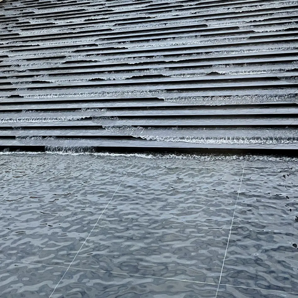 Thin sheets of water cascade down broad, dark stone steps into a rippling tiled pool.