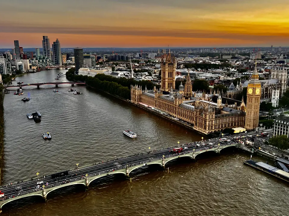 The Palace of Westminster and Elizabeth Tower stand beside the River Thames as Westminster Bridge carries traffic beneath a glowing sunset sky.