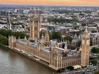 An aerial view shows the Palace of Westminster and its clock tower beside the River Thames at sunset.
