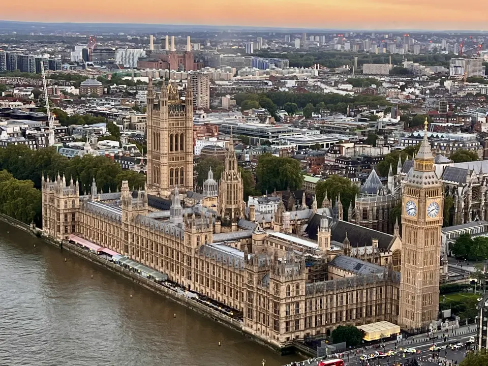 An aerial view shows the Palace of Westminster and its clock tower beside the River Thames at sunset.