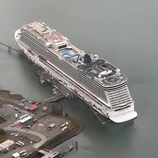 The Norwegian Encore cruise ship is docked beside a pier in calm gray water, viewed from above.