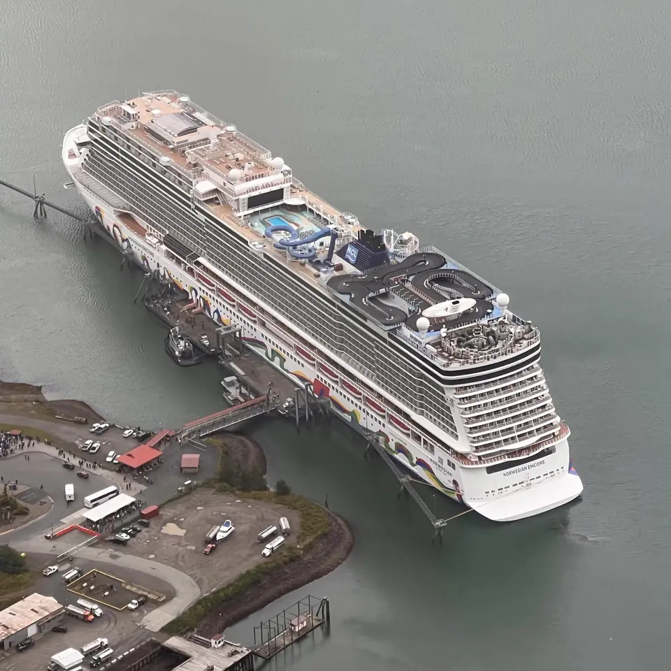 The Norwegian Encore cruise ship is docked beside a pier in calm gray water, viewed from above.