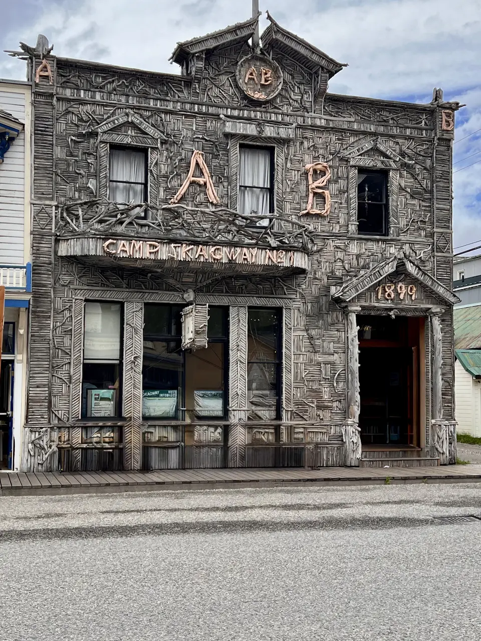A dark, heavily carved wooden building facade with large decorative letters, curtained windows, and the address number 1849 faces a quiet street.