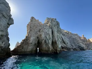 El Arco de Cabo San Lucas rises above clear turquoise water beneath a cloudless blue sky.
