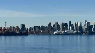 A skyline of high-rise buildings and port cranes stretches along the waterfront beneath a clear blue sky.
