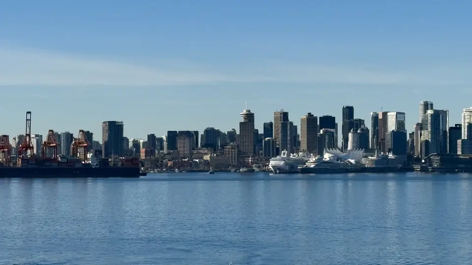 A skyline of high-rise buildings and port cranes stretches along the waterfront beneath a clear blue sky.