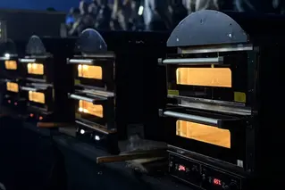 A row of black commercial ovens glows orange through their glass doors in a dim interior.