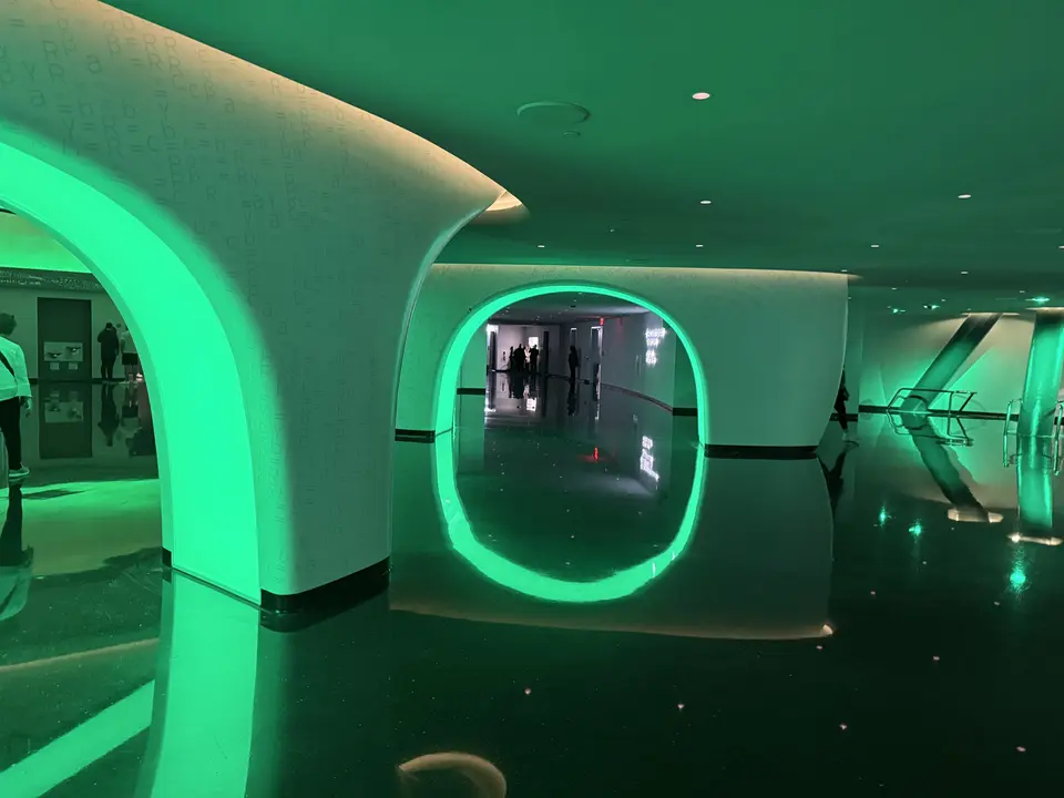 A futuristic interior corridor features glowing green circular archways reflected on a dark polished floor.