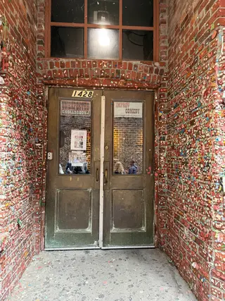 A weathered double door sits between brick walls densely covered in colorful pieces of chewing gum.