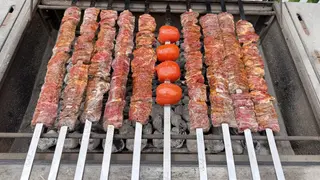 Meat skewers and tomatoes cooking on a grill over charcoal.