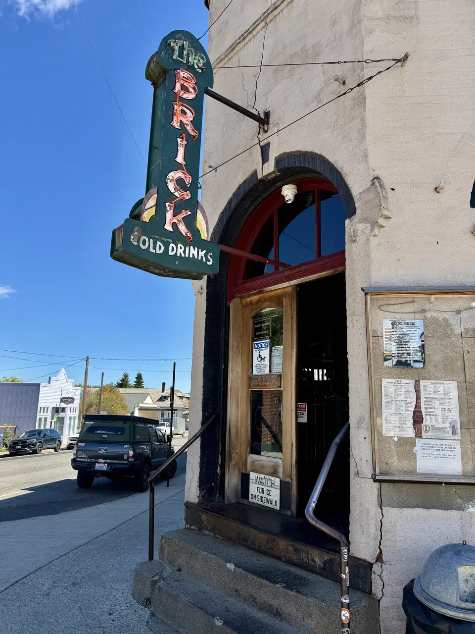 A green sign with red letters hangs above a wooden door on a stone building.