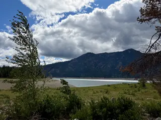 A lake surrounded by mountains and trees under a cloudy sky.