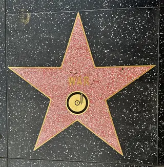 A red terrazzo star with the name "WAR" and a gold record emblem is set into a black speckled sidewalk.