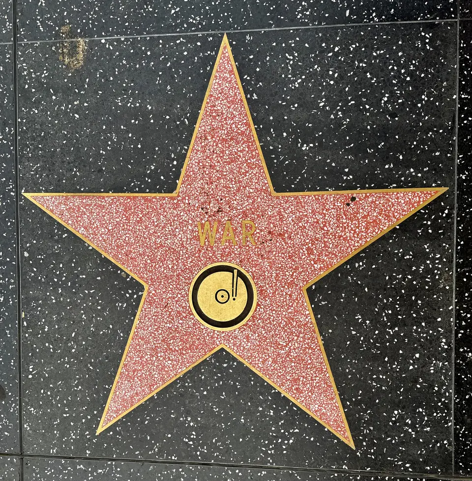 A red terrazzo star with the name "WAR" and a gold record emblem is set into a black speckled sidewalk.