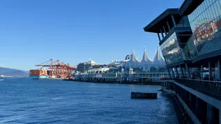 Canada Place and a cruise ship line the waterfront beside container cranes and modern glass buildings under a clear blue sky.
