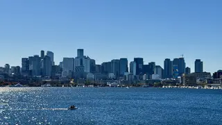 Seattle's downtown skyline rises beyond sparkling blue water, with a small rowboat in the foreground.
